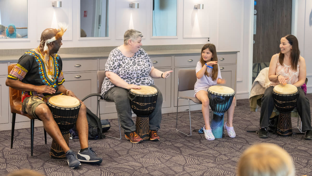 Three adults and a child play traditional African drums at Community Festival 2024