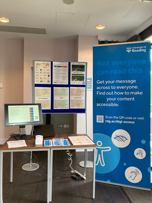 Digital accessibility stall at the Teaching and learning summer event for 2023. A blue retractable pullup roll banner and various posters are displayed. On a table there are more posters and a computer monitor.