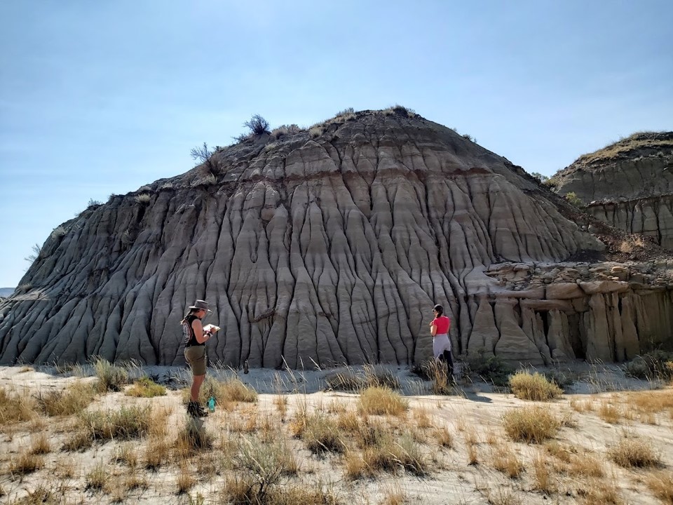 Terie Kaskie and Melissa Dergousoff standing next to the hill containing the hadrosaur skeleton