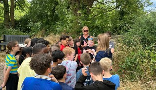 A group of school children in a woodland setting listening to a teacher