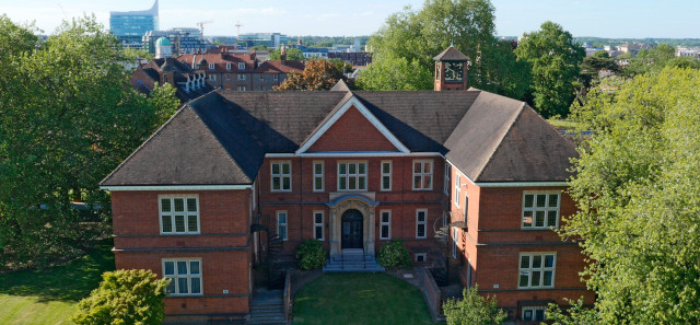 The architecture building at the University of Reading's London Road campus. Trees stand on either side of the building and the sky is blue behind.