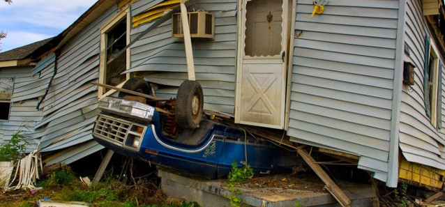A car squashed underneath a wooden house.