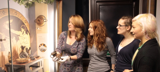 Dr Rhi Smith showing three students objects form the URE Museum of Greek Archaeology