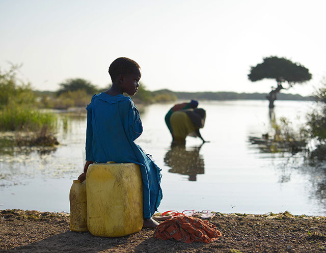 Child waits at lake to fill up water jugs